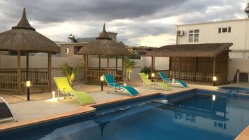 A swimming pool with lounge chairs and thatched umbrellas.