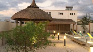 A resort with a thatched-roof structure, a pool area with lounge chairs, and a building with a flat roof. - L'Oiseau de l'Océan (Flic-en-Flac)
