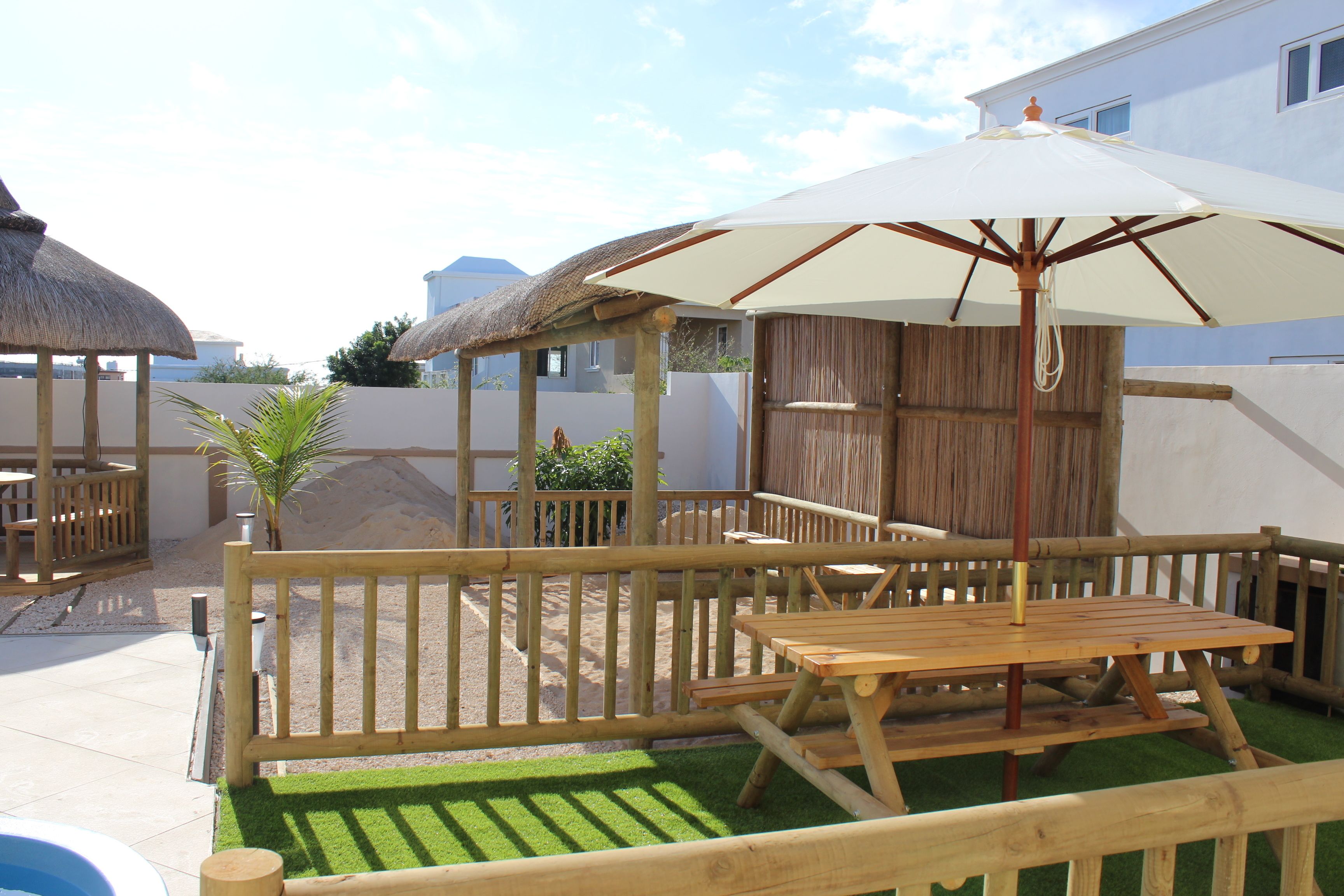 A wooden deck with a table and chairs, a thatched-roof structure, and a white umbrella.