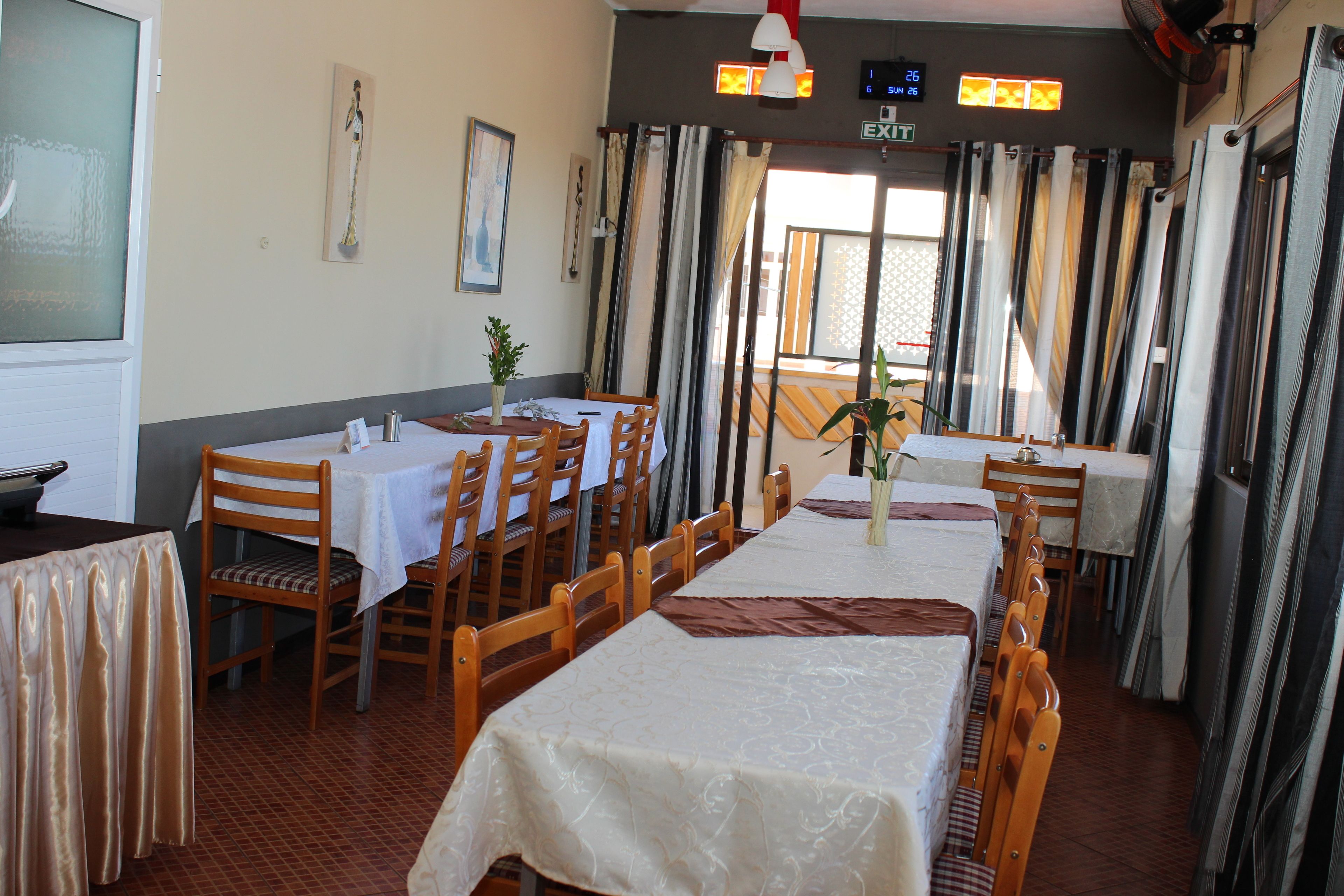 Een restaurant met meerdere tafels en stoelen, een klok en uitzicht op het buiten.