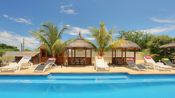 A swimming pool with lounge chairs and thatched-roof structures. - L'Oiseau de l'Océan (Flic-en-Flac)