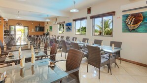 A spacious dining area with high tables and wicker chairs, large windows with views of palm trees, and artwork on the walls. - L'Oiseau de l'Océan (Flic-en-Flac)