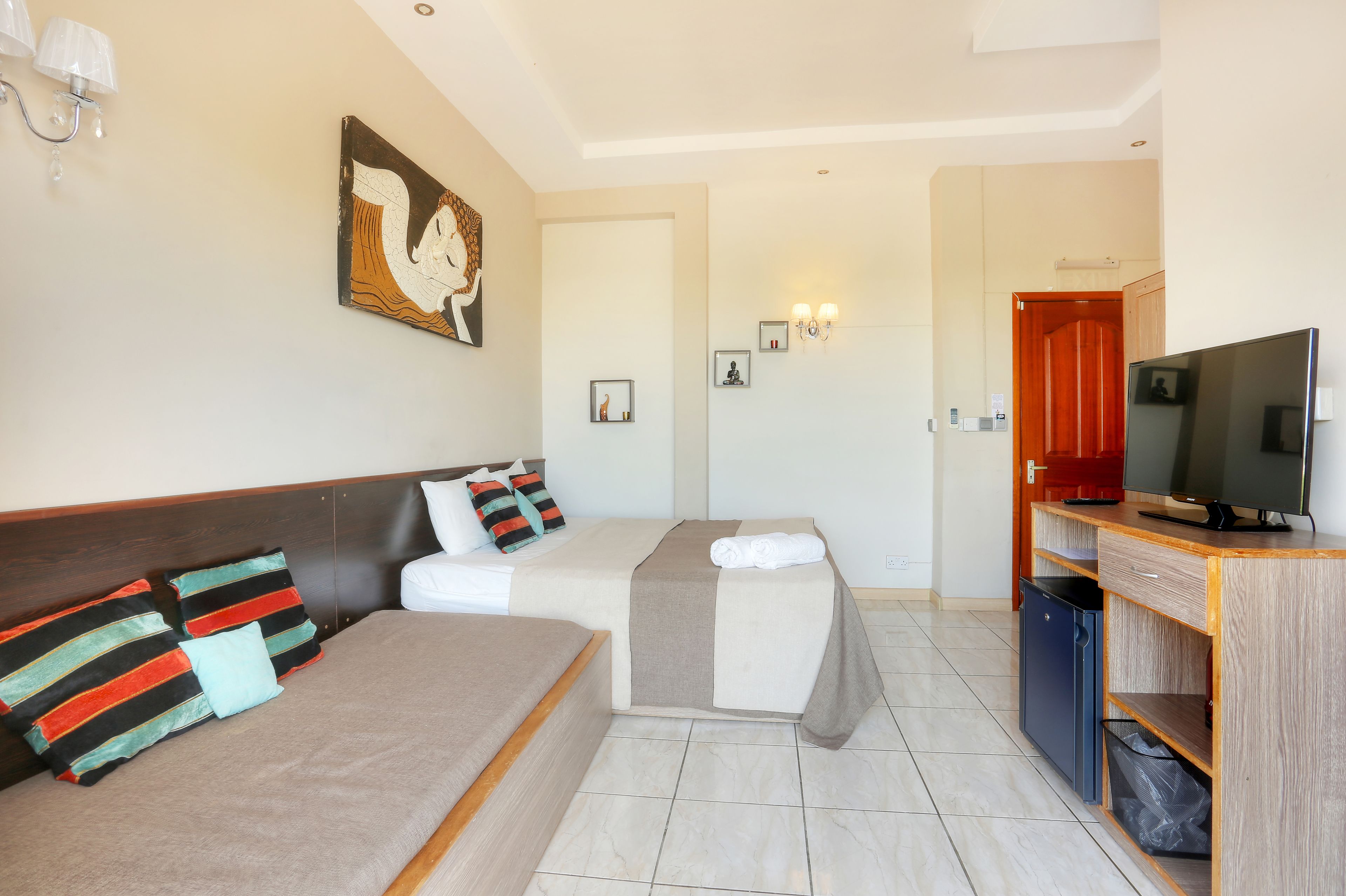 A hotel room with a bed, a sofa, a TV, and a small kitchenette.