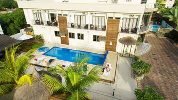 Un hotel con piscina, mobiliario exterior y una estructura de techo de paja.