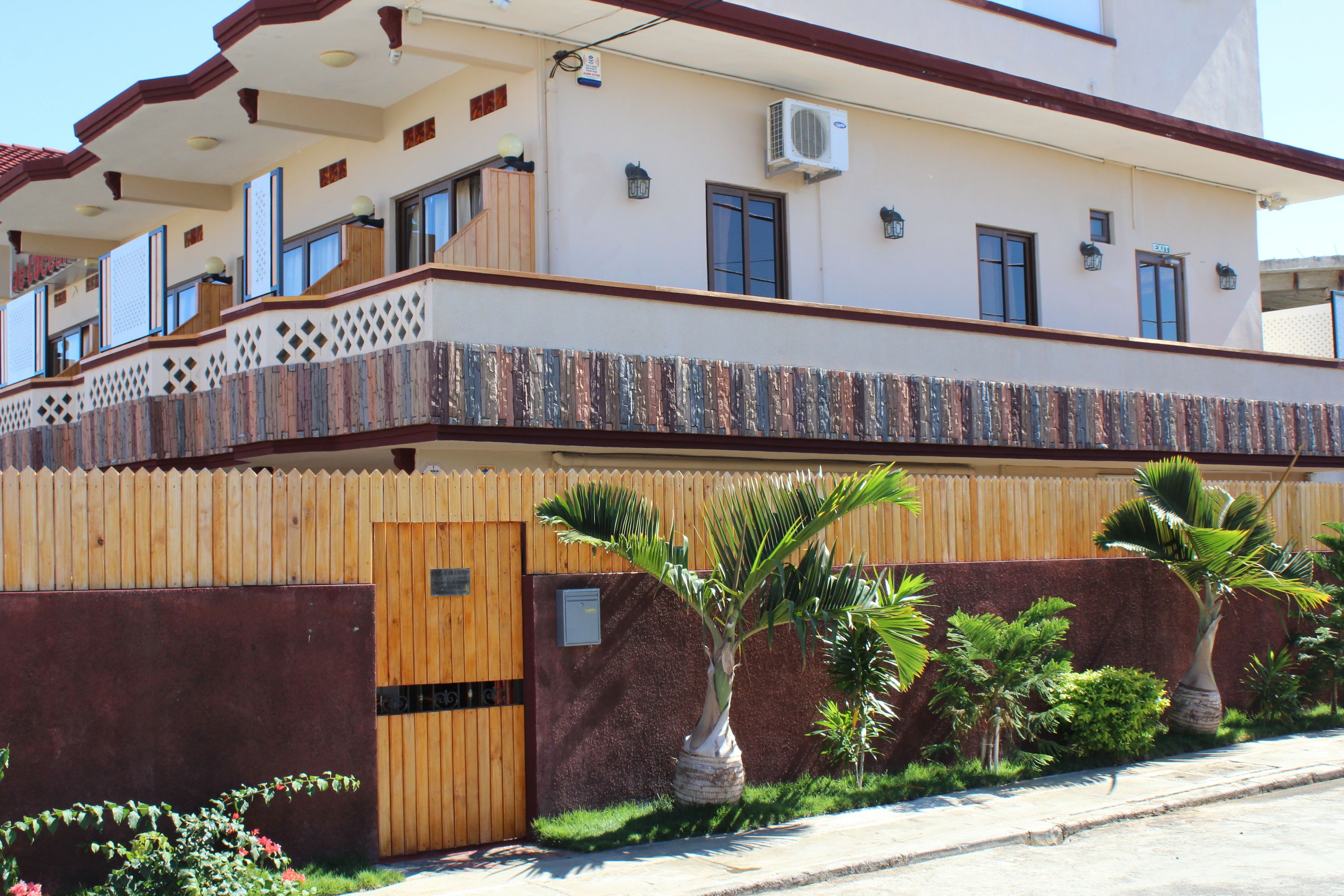 A two-story building with a wooden fence, a balcony, and several potted plants.