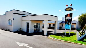 A motel with a signboard, a parking lot, and a building with a flat roof. - Ann’s Volcanic Motel (Rotorua)
