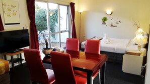 A room with a TV, red chairs, a white sofa, and a dining table. - Ann’s Volcanic Motel (Rotorua)