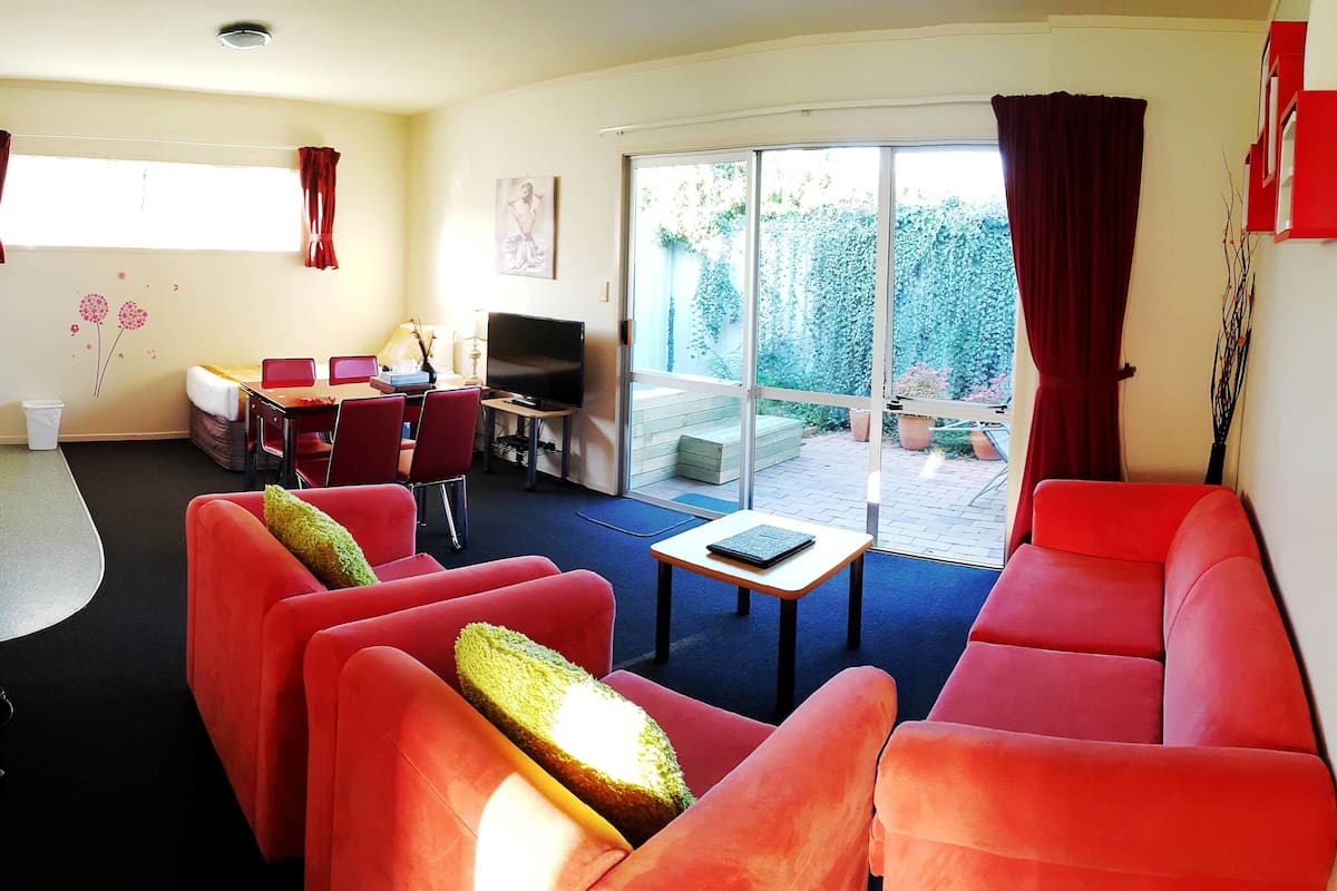 A living room with red sofas, a TV, and a dining area with a table and chairs.