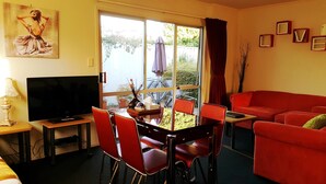 A living room with a red sofa, a dining table with chairs, a TV, and a painting on the wall. - Ann’s Volcanic Motel (Rotorua)