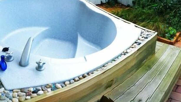 A hot tub with a wooden edge, a faucet, and a small blue bottle on the left. - Ann’s Volcanic Motel (Rotorua)