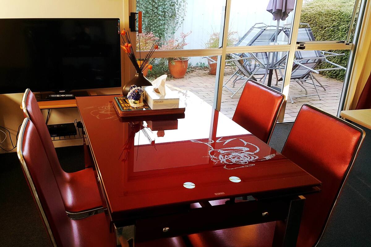 A dining area with a red table, four red chairs, a television, and a window with a view of the outdoors.