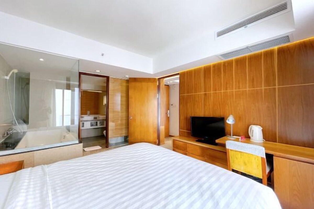 Habitación de hotel moderna con una cama grande, televisión, escritorio con lámpara y zona de ducha.