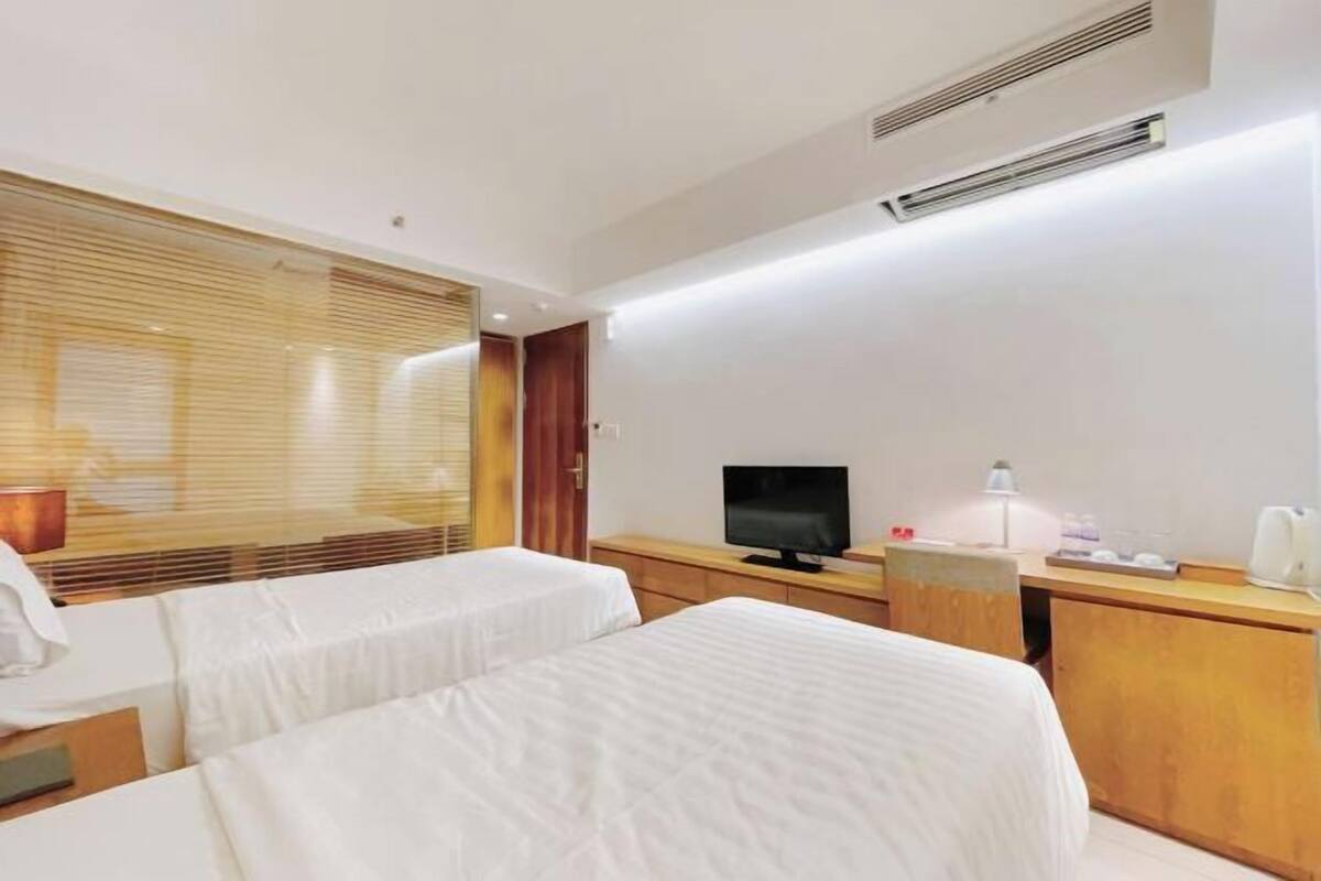 Een hotelkamer met twee bedden, een televisie, een bureau en een raam met jaloezieën.