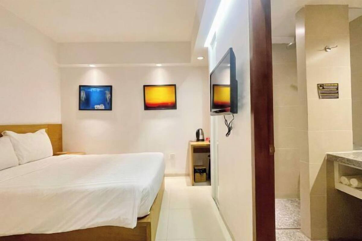 Een hotelkamer met een bed, een aan de muur bevestigde televisie en een klein kastje met toiletartikelen.