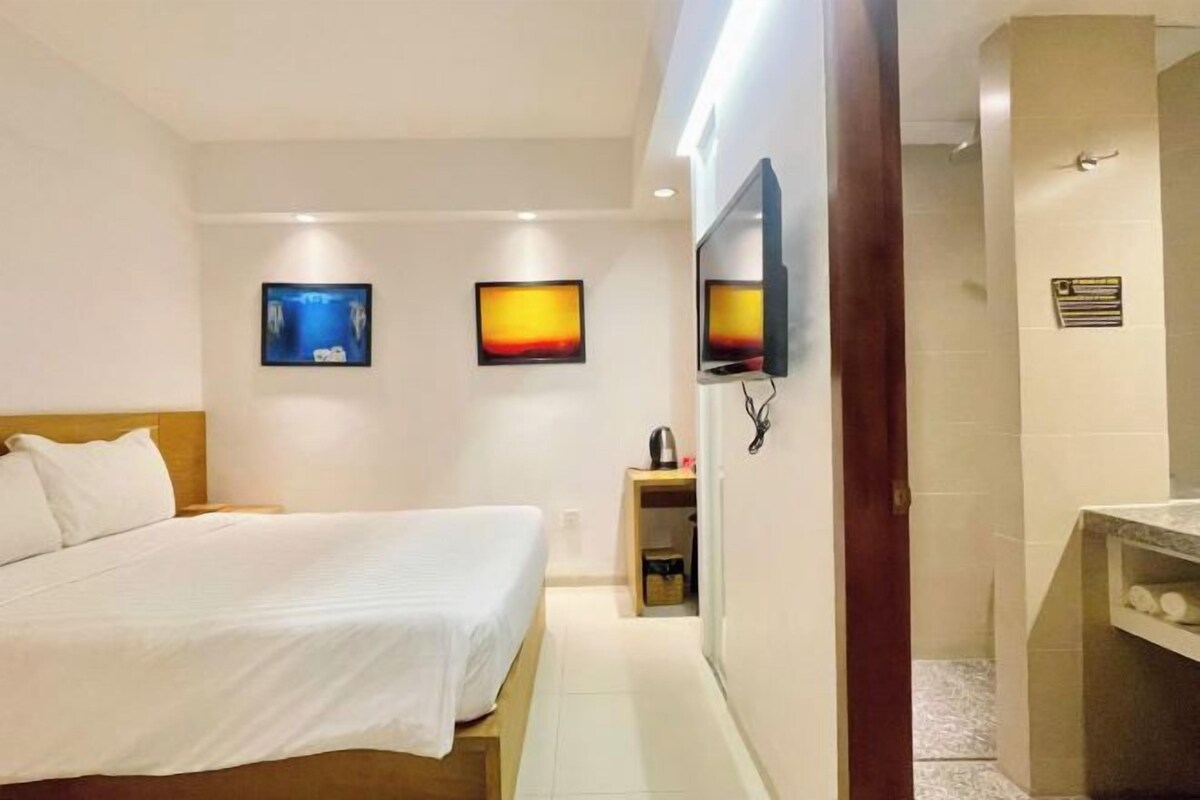 Habitación de hotel con una cama, televisor montado en la pared y un mueble pequeño con artículos de aseo.
