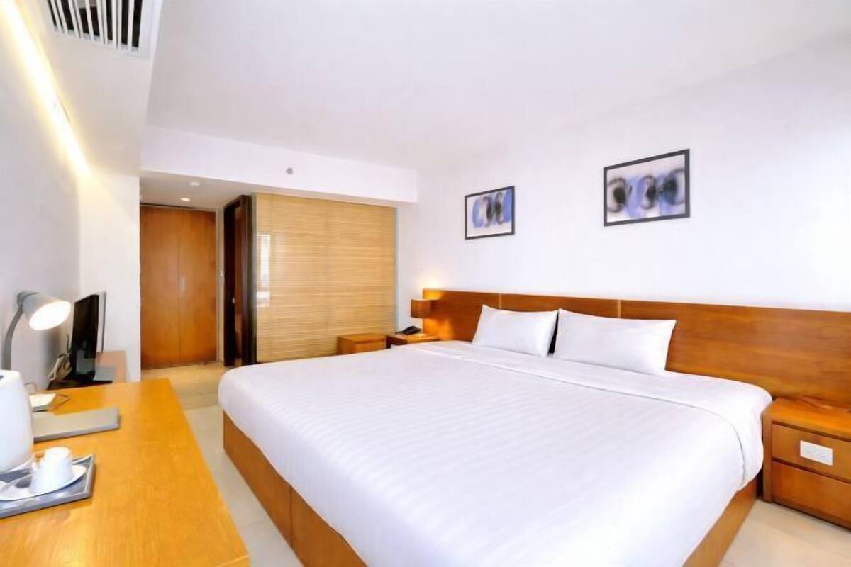 Een hotelkamer met een groot bed, nachtkastjes, een bureau met lamp en een houten garderobe.