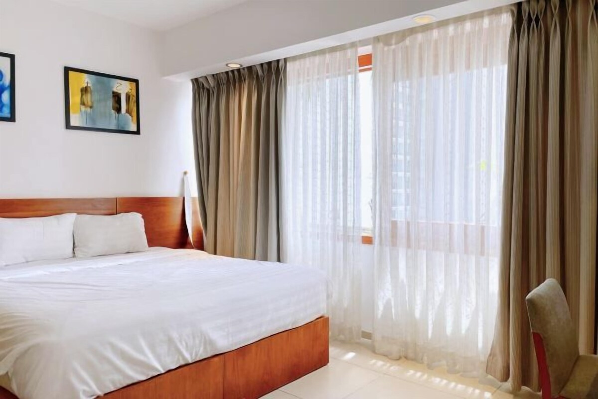 Habitación de hotel con una cama grande, cabecera de madera, cortinas translúcidas y dos cuadros en la pared.