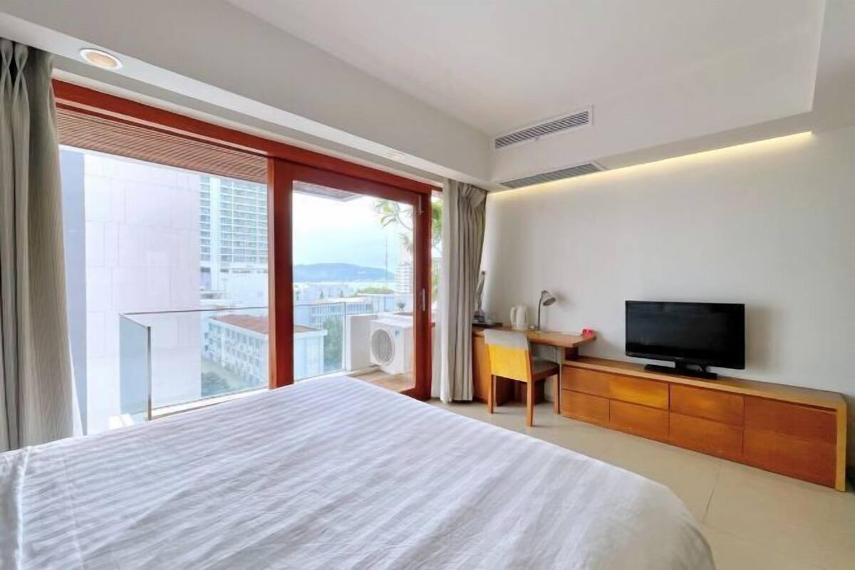 Een hotelkamer met een groot bed, een bureau met een stoel, een televisie en een schuifdeur naar een balkon.