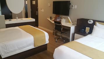 A hotel room with two beds, a desk, a chair, a TV, and a small plant.