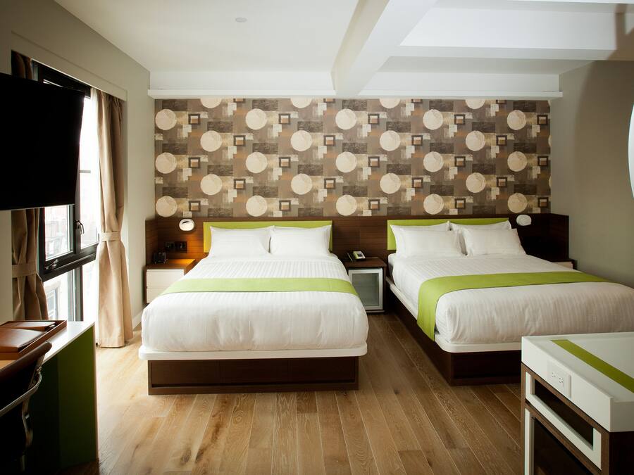 A hotel room with two beds, a desk, a TV, and a patterned wall.