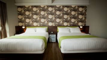 A hotel room with two beds, a patterned wall, and a small bedside table with a lamp.