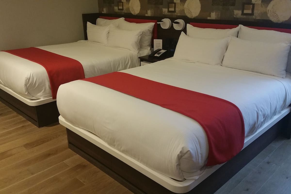 Two double beds with red and white bedding, wooden flooring, and a nightstand with a phone.