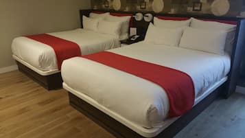 Dos camas matrimoniales con ropa de cama roja y blanca, suelo de madera y una mesita de noche con un teléfono.