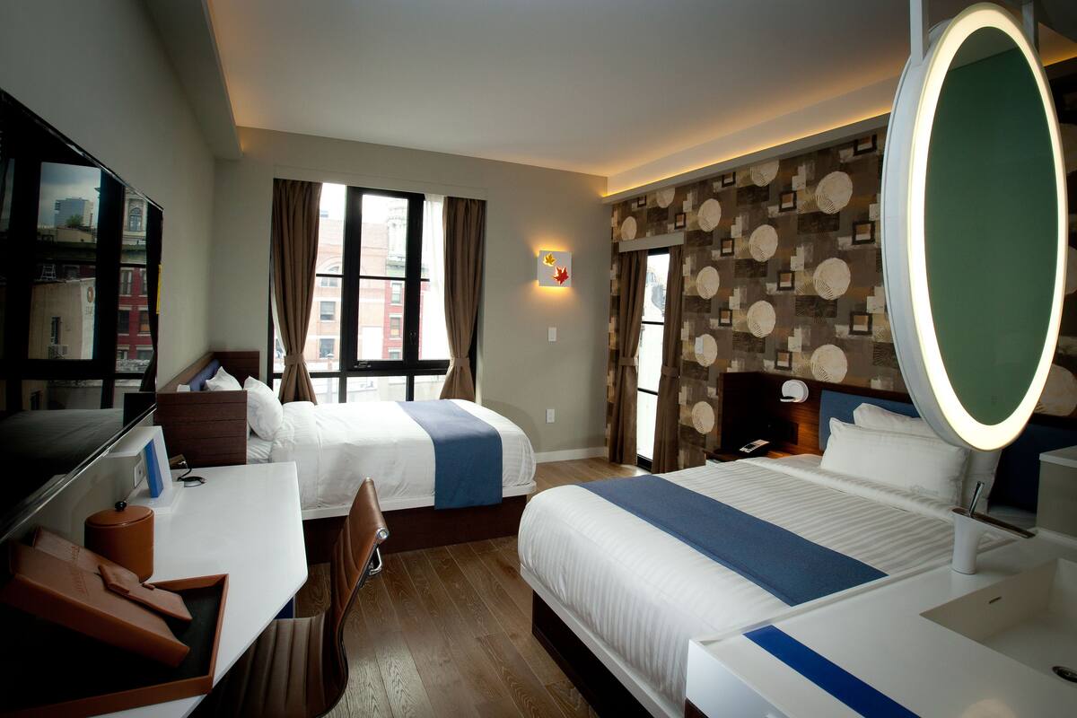 A hotel room with two beds, a desk, a chair, a large mirror, and a window with curtains.