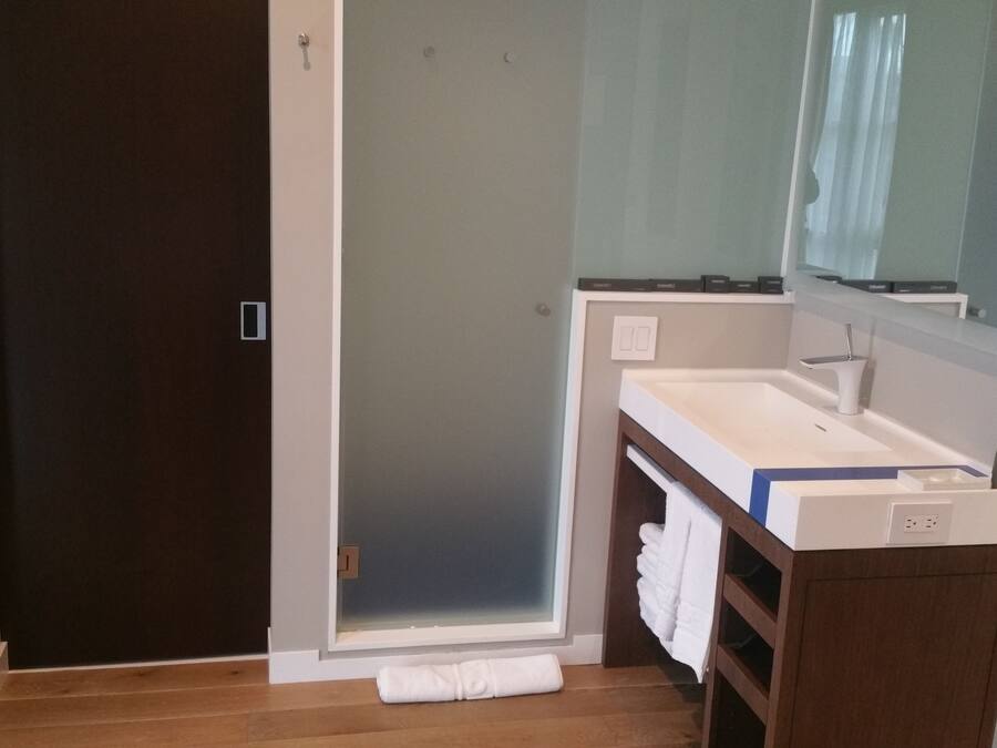 Un baño con una puerta oscura, un lavamanos blanco, un espejo y una toalla en el suelo.