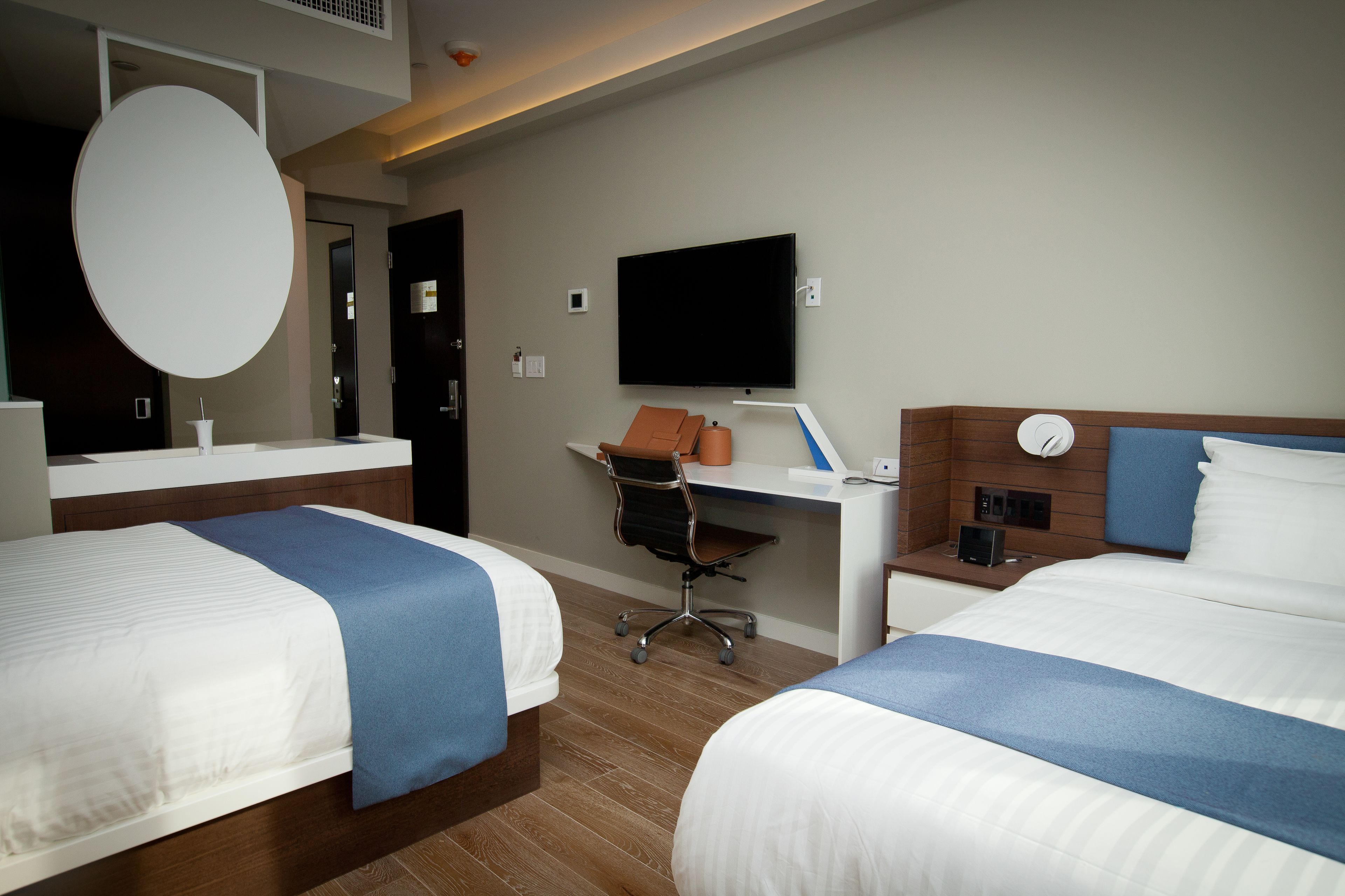 A hotel room with two beds, a desk, a chair, a television, and a mirror.