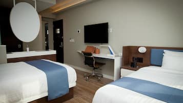A hotel room with two beds, a desk, a chair, a television, and a mirror.