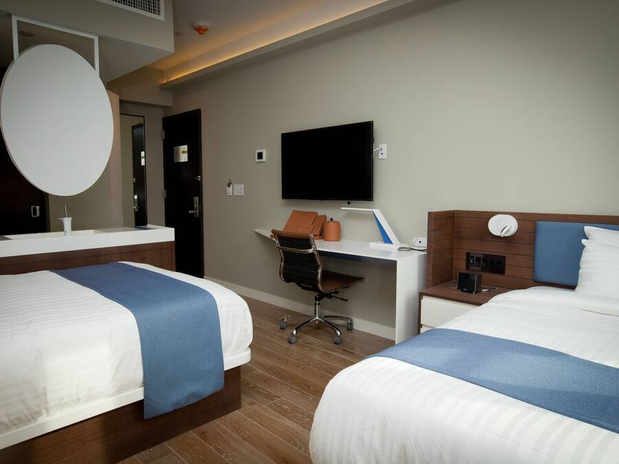 Habitación de hotel con dos camas, un escritorio, una silla, un televisor y un espejo.