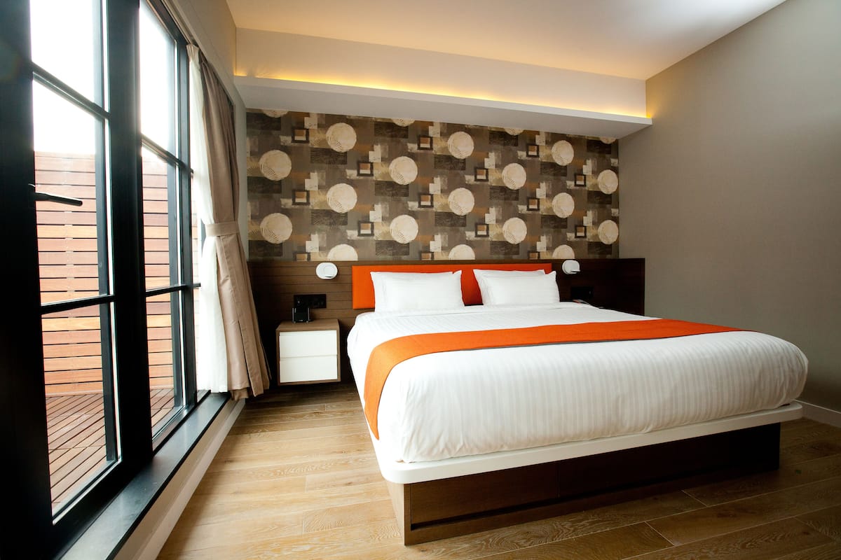 A modern hotel room with a large bed, a nightstand, a wall-mounted lamp, and a window with curtains.