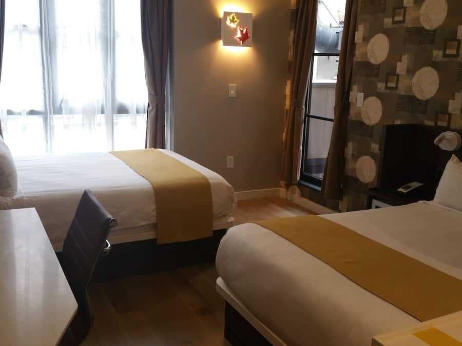 A hotel room with two beds, a desk with a chair, a TV, and a window with curtains.