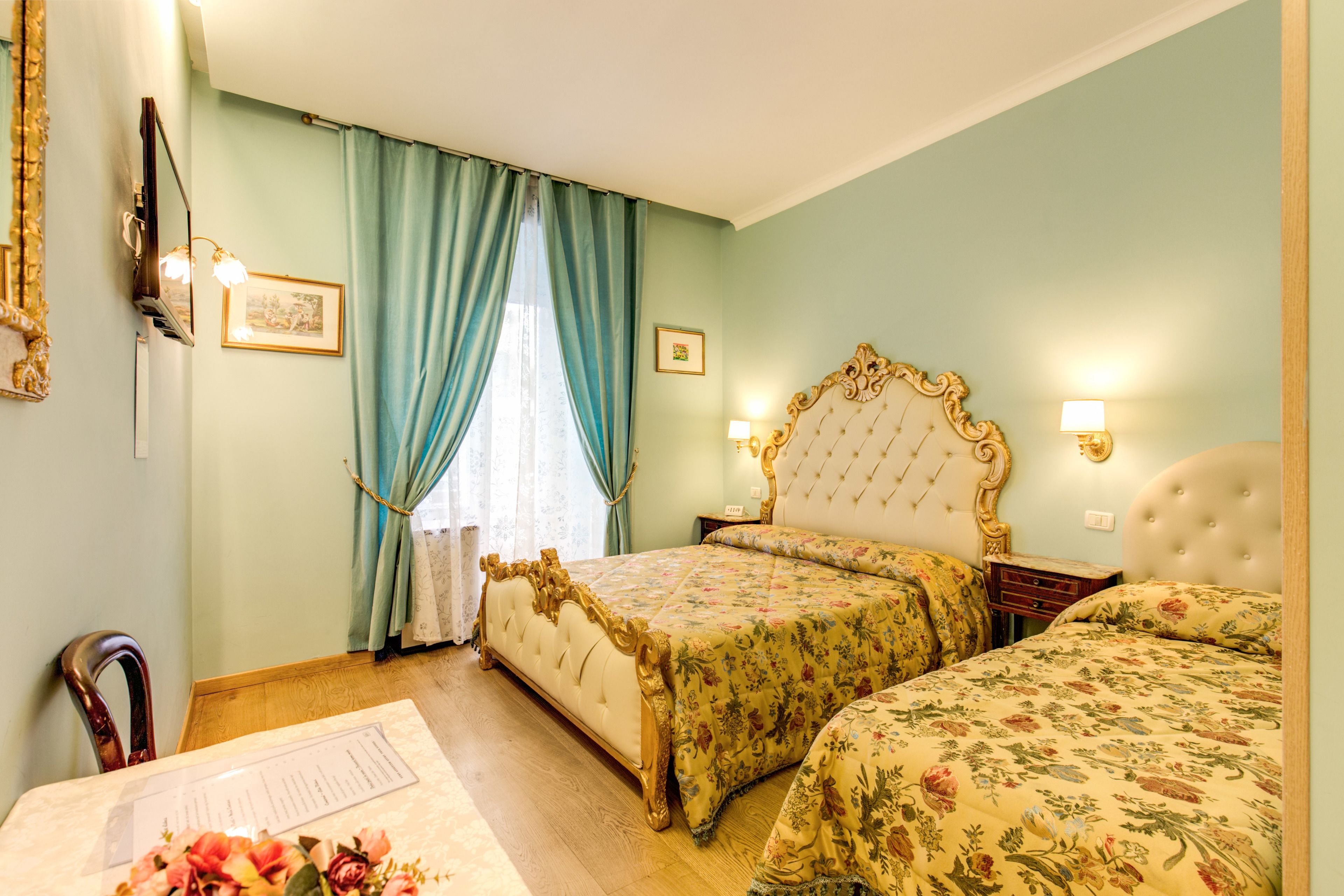 A bedroom with two beds, a wooden chair, a desk with a chair, and a window with curtains.