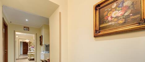 A hallway with a framed floral painting on the wall, a vase with flowers, and a door at the end.