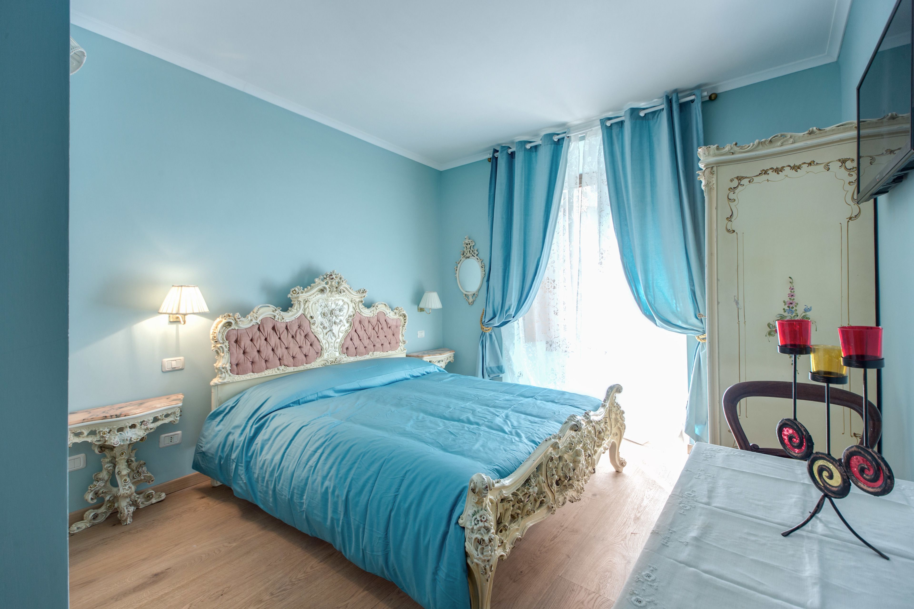 Un dormitorio con cama, mesita de noche, cómoda, espejo y ventana con cortinas.