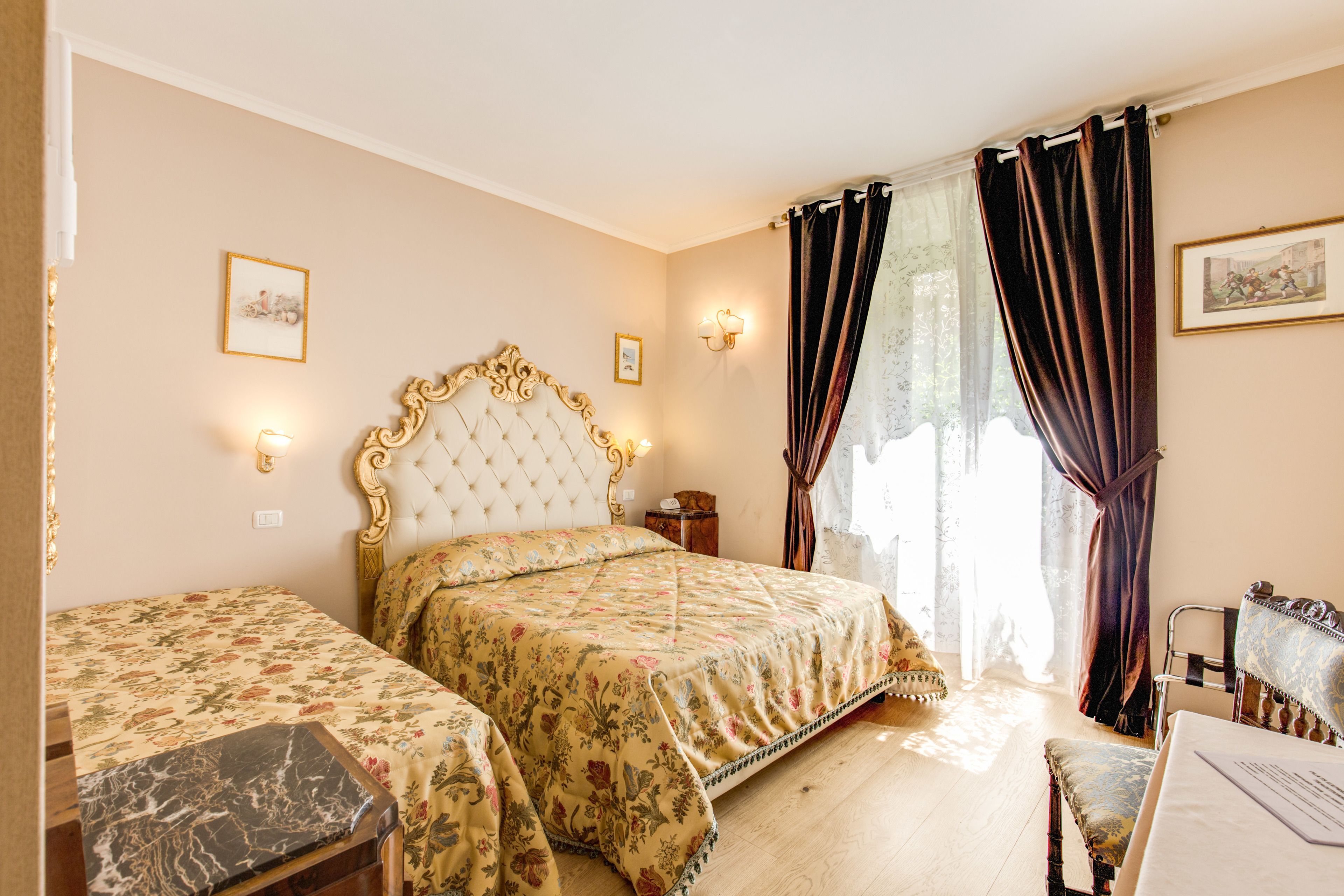 A bedroom with two beds, a wooden floor, a desk with a chair, and a window with curtains.