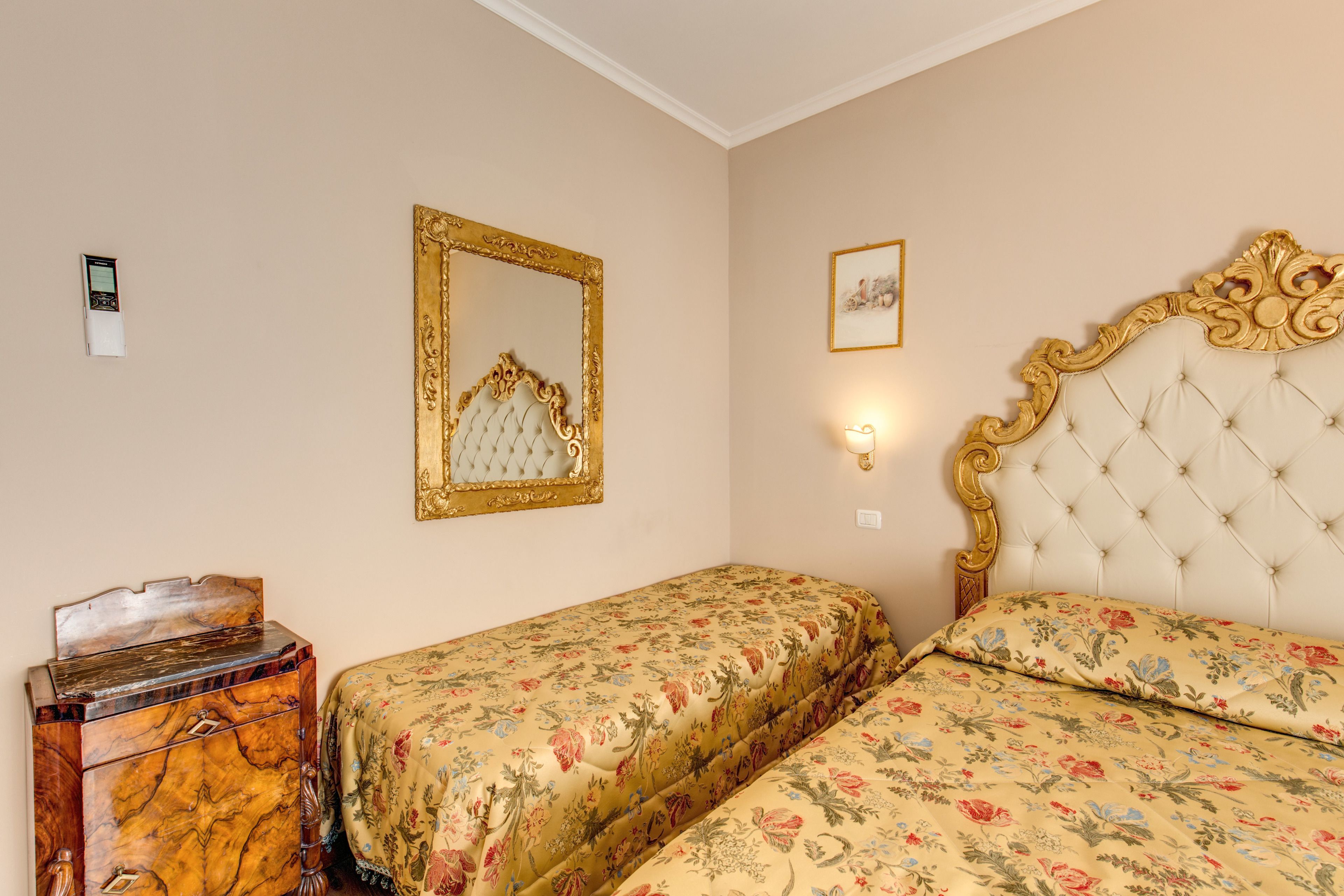A hotel room with two beds, a wooden dresser, a gold-framed mirror, and a framed picture on the wall.