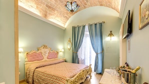 A bedroom with a large bed, a chandelier, a table with a bottle of champagne, and a TV on the wall. - La Reggia dei Principi (Rome)