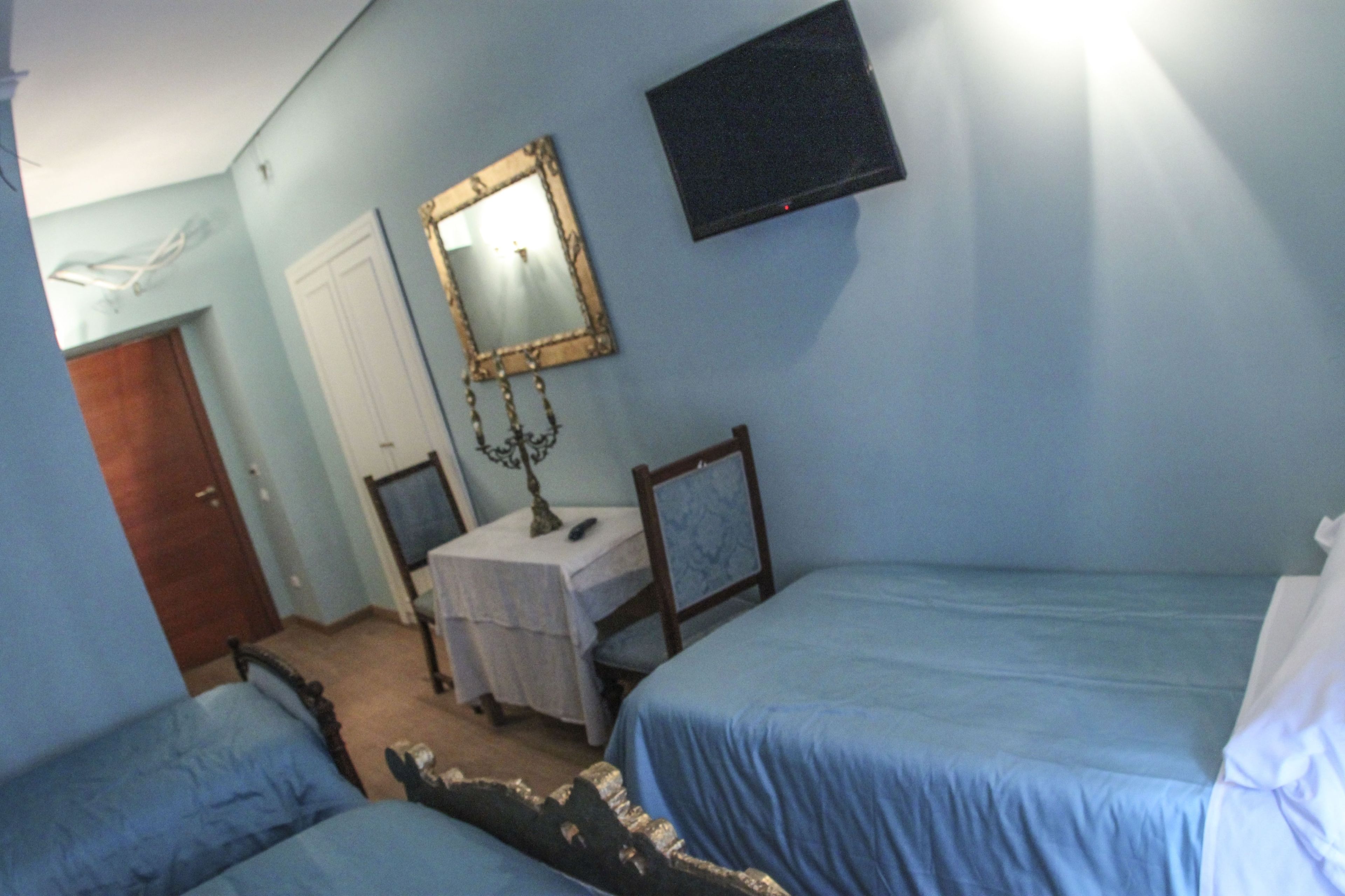 A bedroom with two beds, a bedside table, a mirror, a TV, and a door.