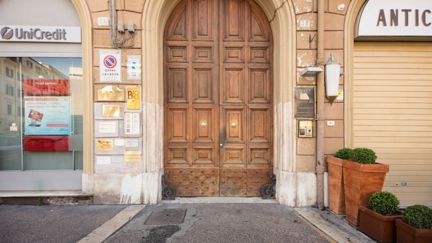 A large wooden double door with a plaque, a UniCredit sign, and a no parking sign. - La Reggia dei Principi (Rome)