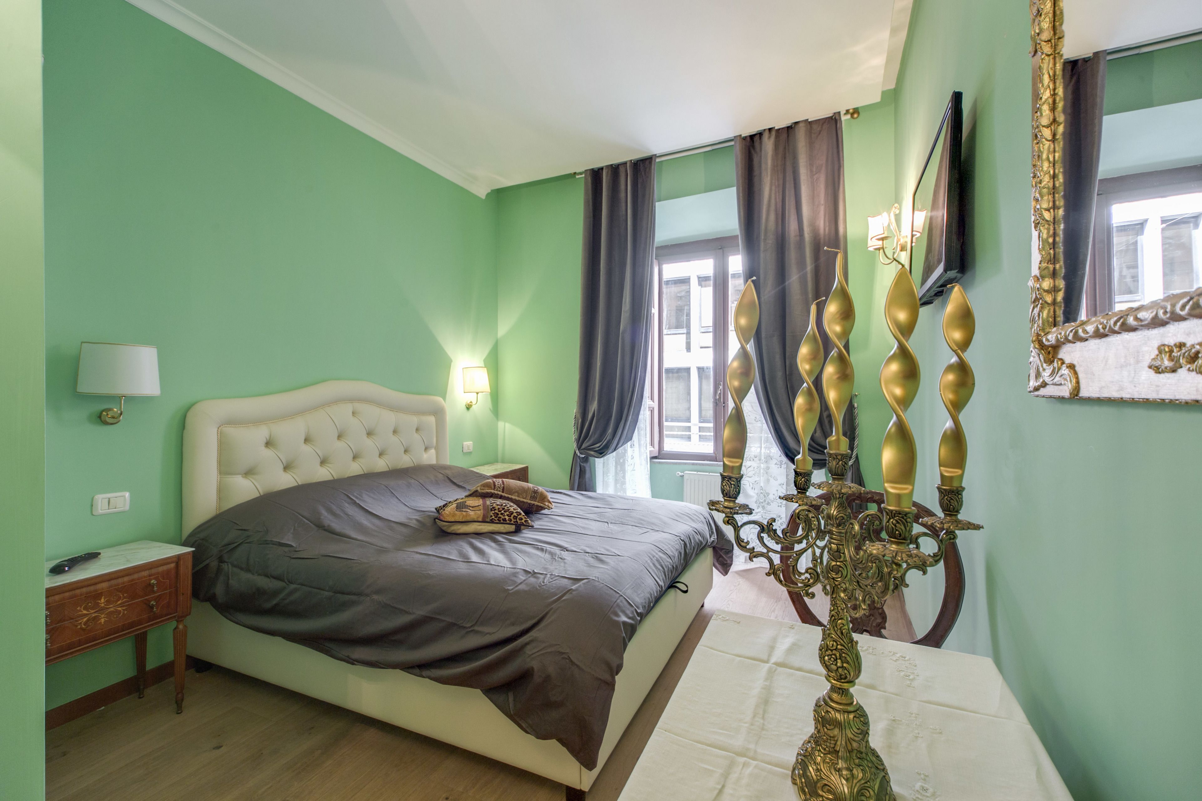 A bedroom with a bed, nightstand, lamp, curtains, and a decorative candelabra.