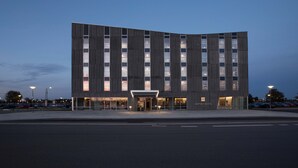 Un hôtel moderne à la façade incurvée, doté de grandes fenêtres et d’une entrée bien éclairée.