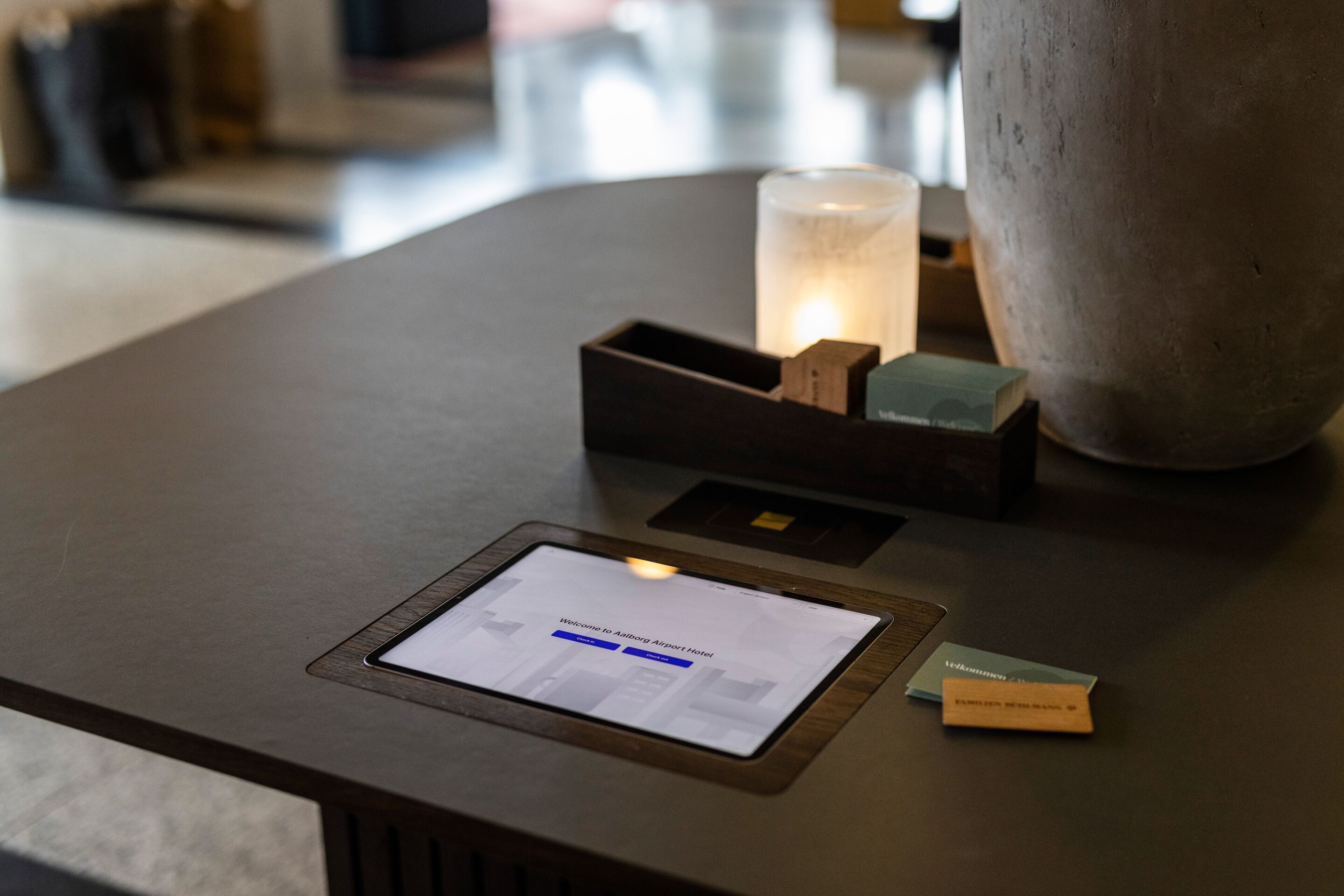 A reception desk with a digital display, a candle, and a large vase.