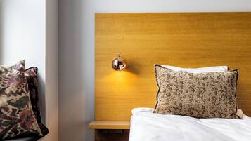Cama bem arrumada com travesseiro estampado e um travesseiro liso, mesa de cabeceira com objeto decorativo e luminária fixada na parede.
