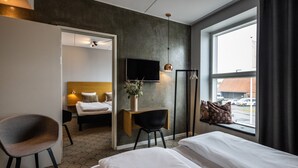 Une chambre d’hôtel comprenant un lit, un bureau avec une chaise, un téléviseur fixé au mur et une fenêtre avec des rideaux.