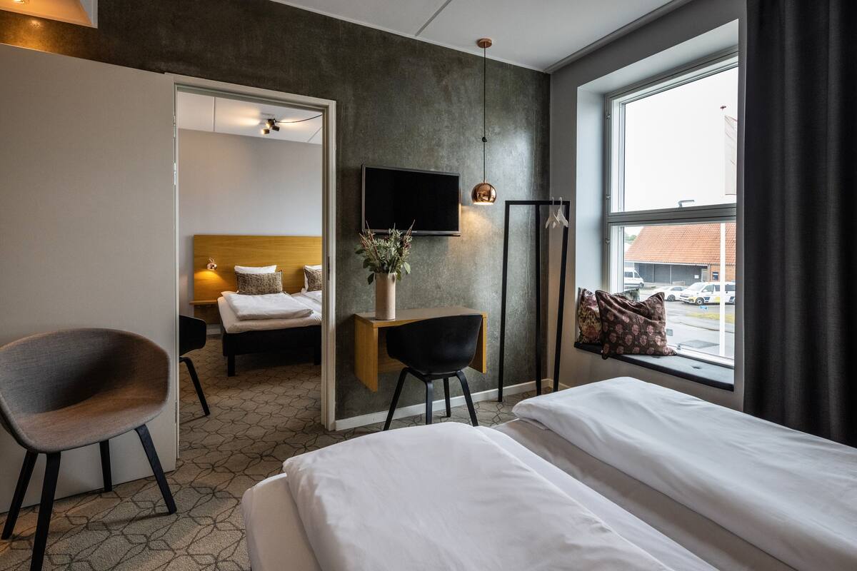 Ein Hotelzimmer mit einem Bett, einem Schreibtisch mit Stuhl, einem an der Wand montierten Fernseher und einem Fenster mit Vorhängen.