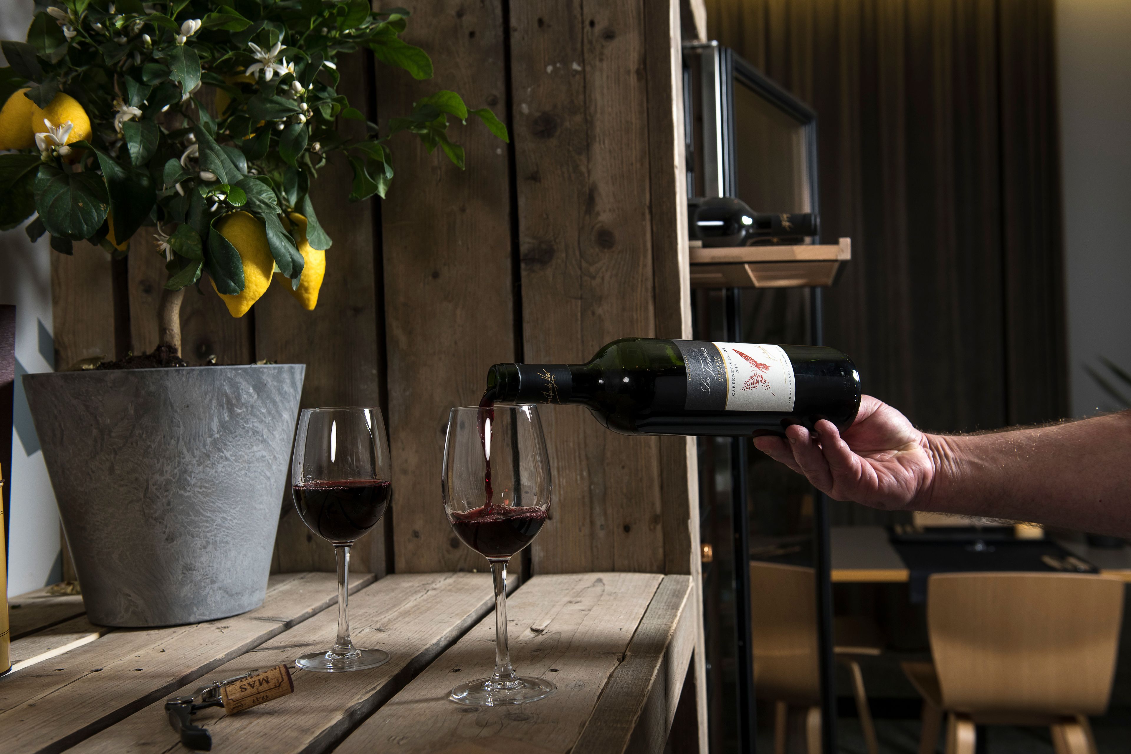 A wooden table with two wine glasses and a bottle of wine being poured into one of them.