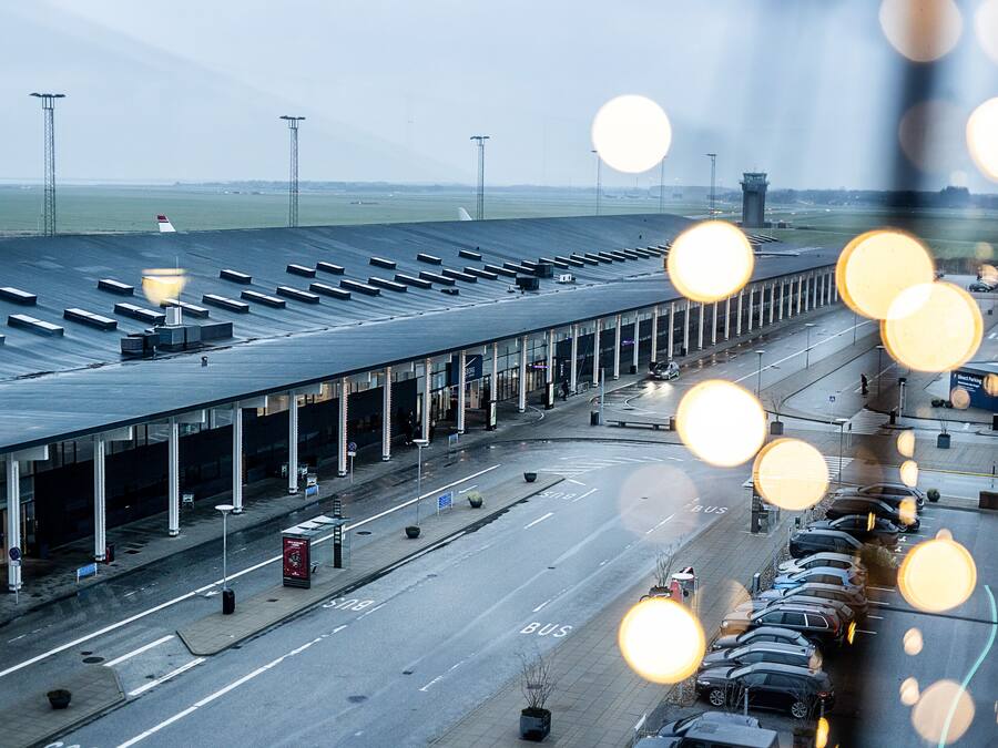 Terminal aeroportuario con varias vías para autobuses y coches, una torre de control y una amplia zona abierta con techo.